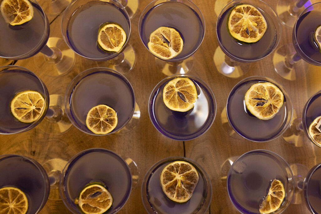 A bird's eye view of cocktail glasses with purple liquid and dried citrus garnishes.